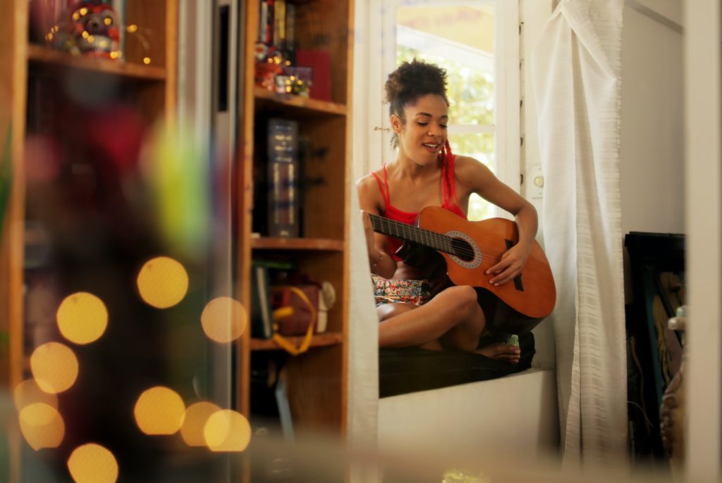 Black Woman Singing And Playing Guitar At Home