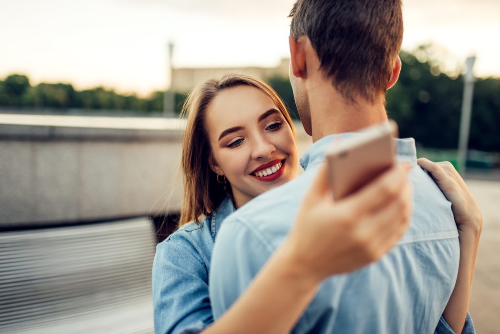 Couple hugs and using gadgets, modern relationship