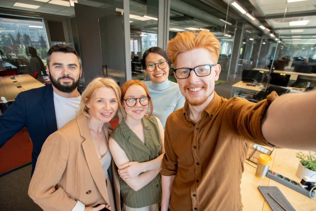 Group of successful office workers with toothy smiles making selfie in office