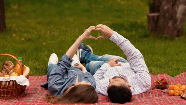 Pair of sweethearts making heart with hands to show their love during picnic at park