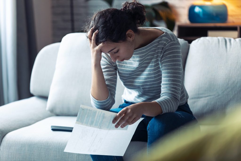 Worried young woman thinking about her problems while holding bills of home.